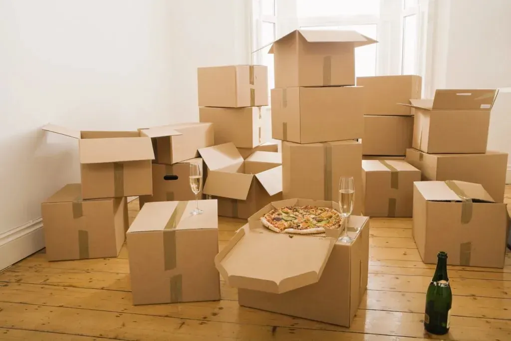 Moving boxes with pizza, champagne and glasses on floor