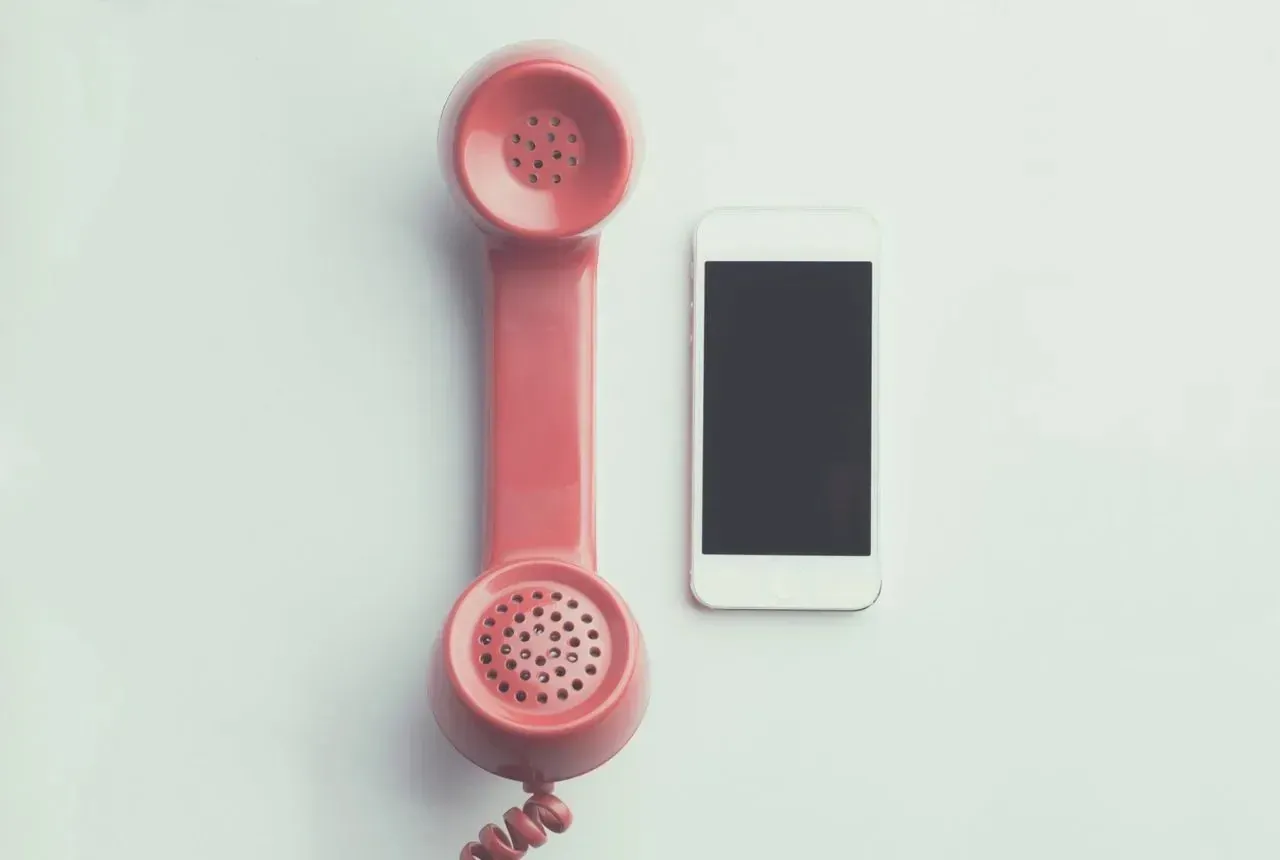 Vintage pink telephone handset beside modern smartphone