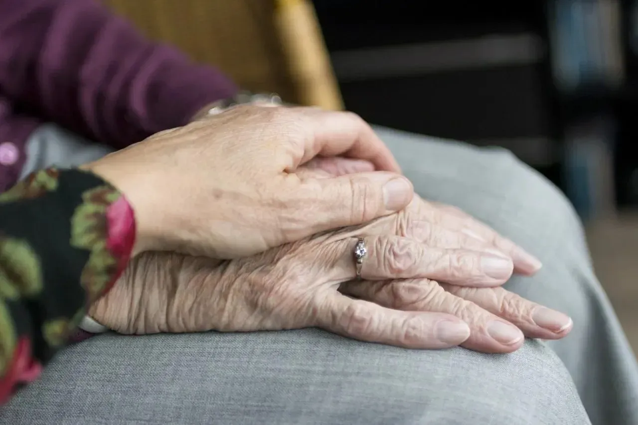 Younger hand resting on elderly person's hands