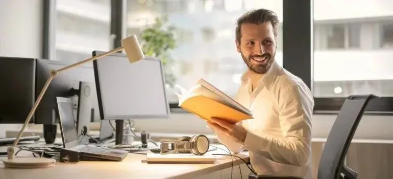Smiling man holding open book at office desk