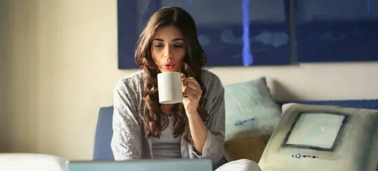 Woman with mug at laptop in bedroom