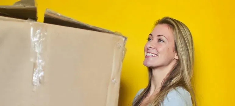Smiling woman carrying cardboard box, yellow background