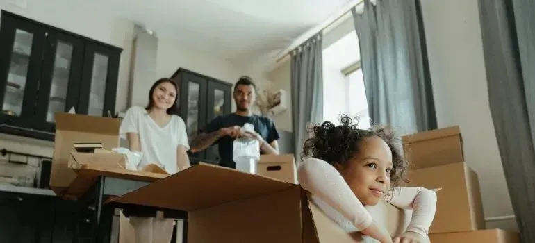 Family unpacking moving boxes, child leaning on box