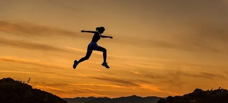Silhouette of woman leaping between rocks at sunset