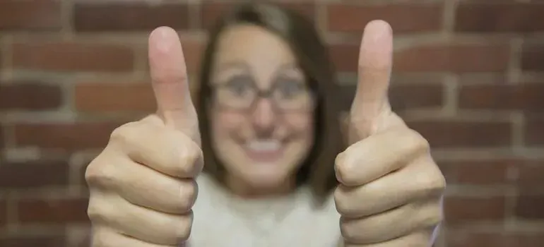 Smiling woman giving two thumbs up, brick background