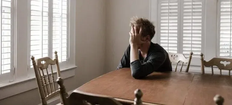 Stressed man at wooden dining table, head in hand