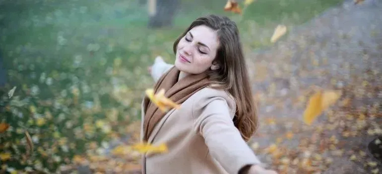 Woman with open arms among falling autumn leaves