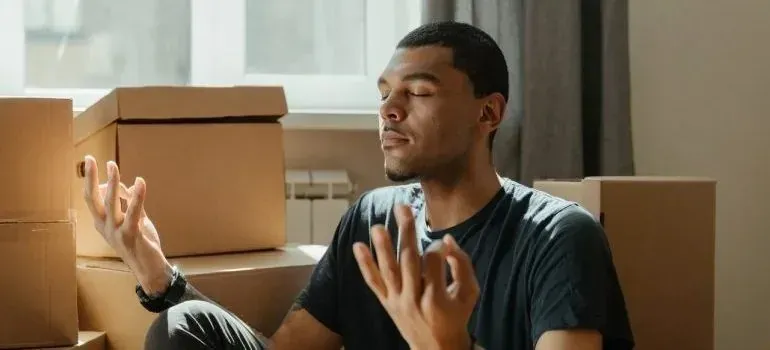 Man meditating cross-legged among cardboard moving boxes