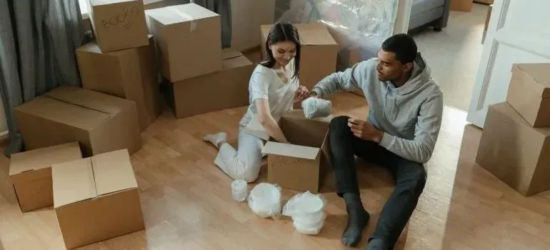 Couple unpacking bubble-wrapped dishes among moving boxes