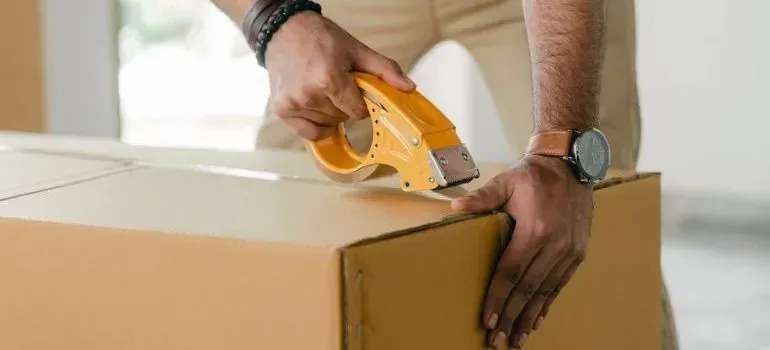 Man sealing cardboard box with yellow tape gun