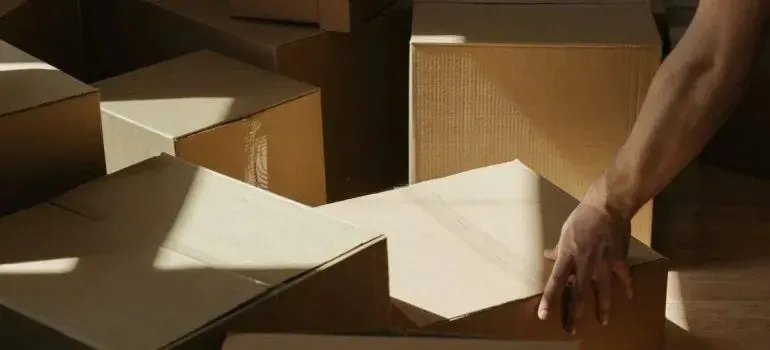 Person handling stacks of plain cardboard boxes in sunlight