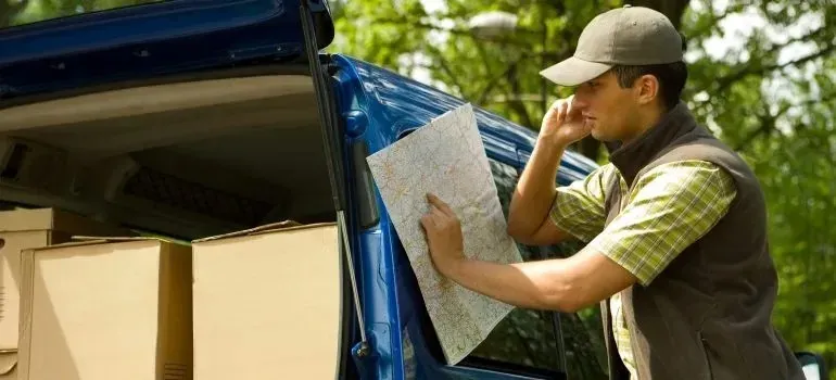 Man reading map beside blue van loaded with boxes