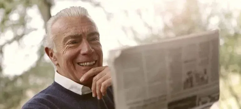 Cheerful senior man reading newspaper outdoors