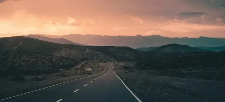Empty highway through mountains under sunset sky