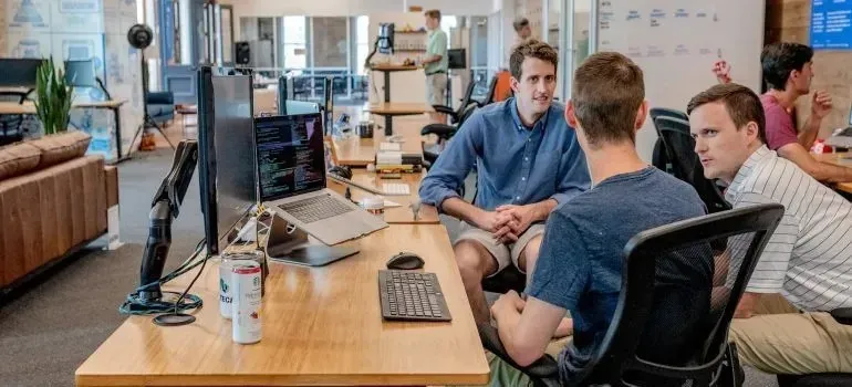 Casual open-plan office, men talking at desks; no identifiable branding