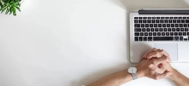 Clasped hands beside laptop keyboard on white desk
