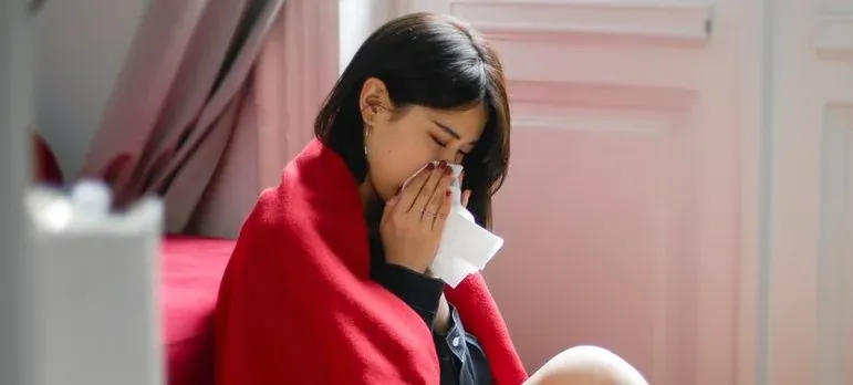 Sick woman in blanket blowing nose