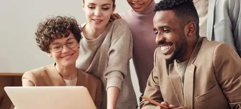 Diverse coworkers smiling around a laptop in bright office