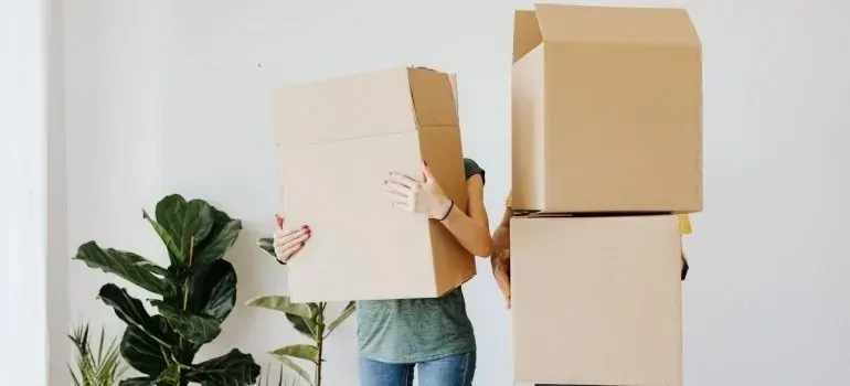 Couple carrying large cardboard moving boxes indoors