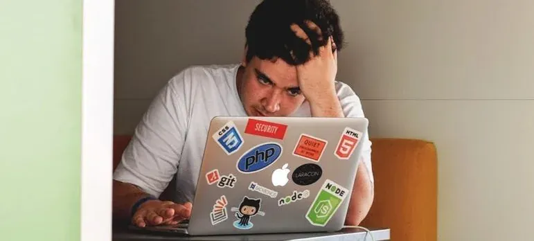 Stressed developer, laptop with tech stickers (PHP, Node), no business branding