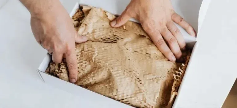 Hands arranging honeycomb packing paper in white box