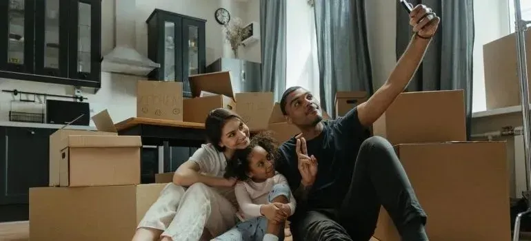 Family selfie on kitchen floor surrounded by moving boxes