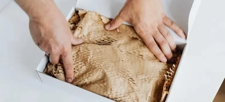 Hands arranging honeycomb packing paper inside white box