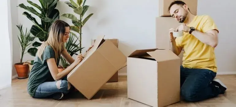 Couple packing cardboard boxes on floor of apartment
