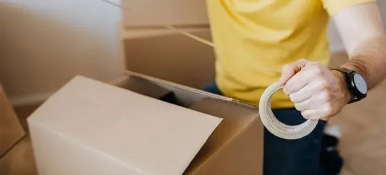 Man in yellow shirt holding tape roll by boxes