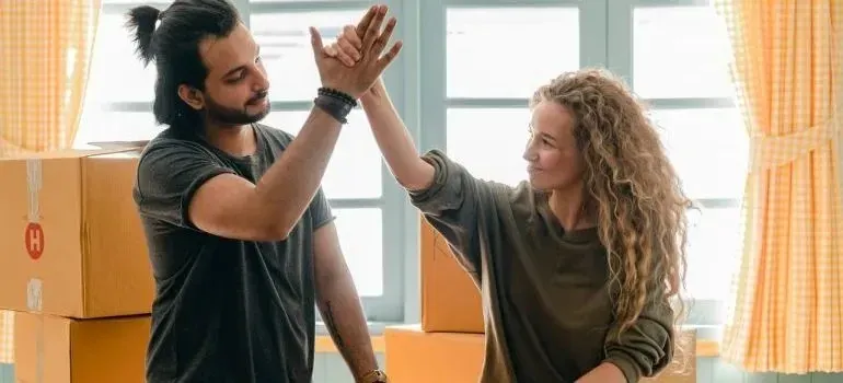 Couple high-fiving between cardboard moving boxes indoors