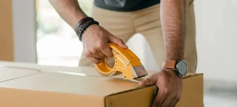 Man sealing cardboard box with yellow tape dispenser