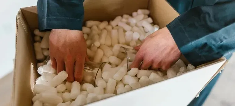 Hands packing glassware into box of foam peanuts