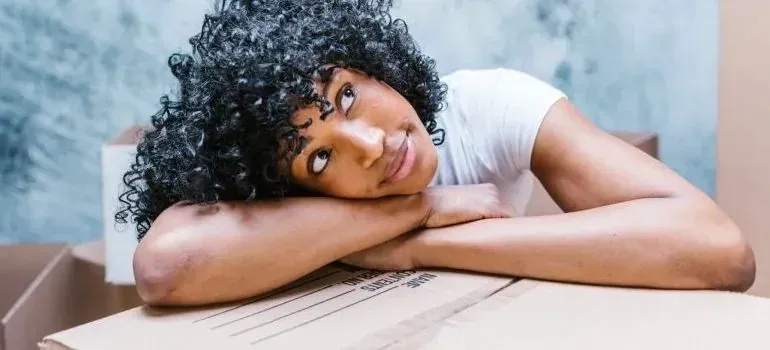 Daydreaming woman resting arms on labeled moving box