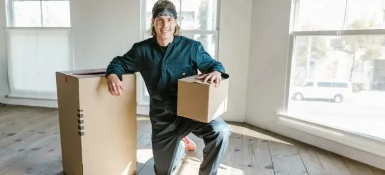 Mover in dark coveralls kneeling beside cardboard boxes