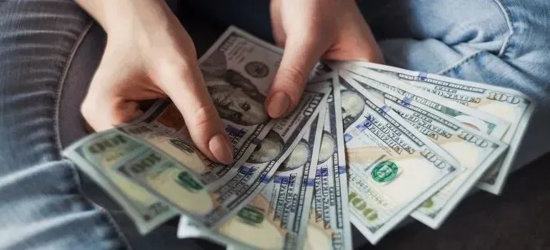 Hands fanning out hundred-dollar bills in lap