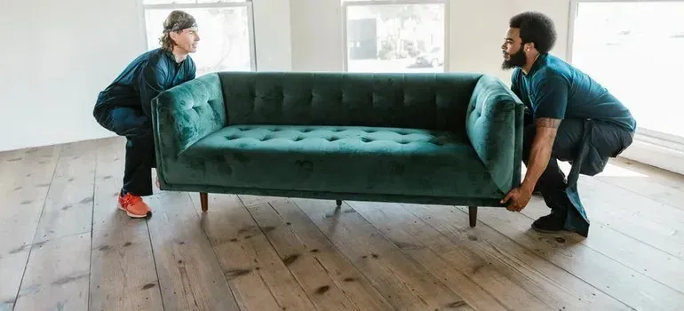 Two movers lifting green velvet sofa in empty room