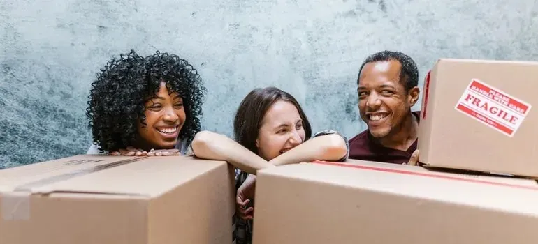 Three happy people peeking over cardboard boxes with fragile stickers