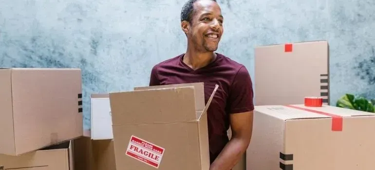 Man carrying cardboard box with fragile sticker among packed boxes