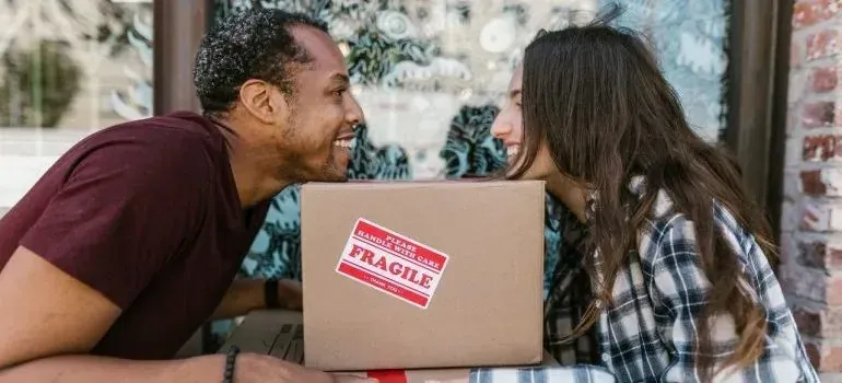Couple smiling face to face over fragile-labeled moving box
