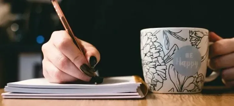 Hand writing in notebook beside floral Be Happy mug