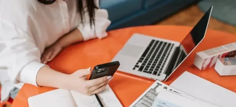 Woman with phone and laptop reviewing documents at orange table