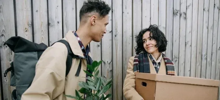 Couple with cardboard box and plant beside wooden fence