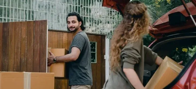 Couple loading cardboard boxes into red car trunk