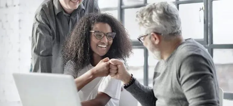 Colleagues fist-bumping over laptop in bright office