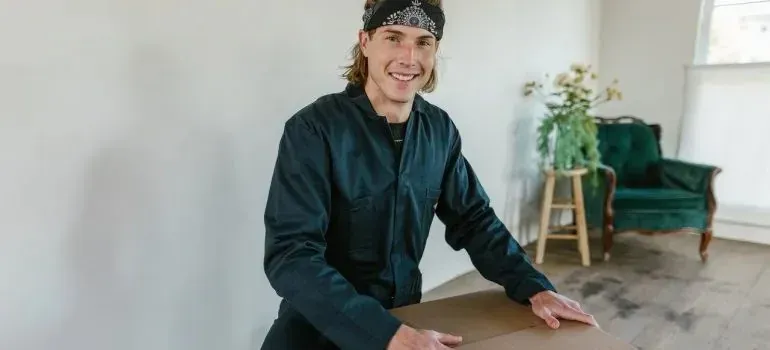 Smiling mover in plain coveralls holding cardboard box