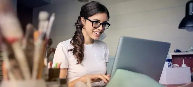 Smiling woman with glasses typing on laptop