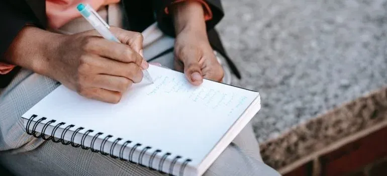 Hands writing in spiral notebook outdoors