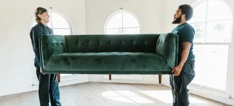 Two movers carrying green velvet sofa