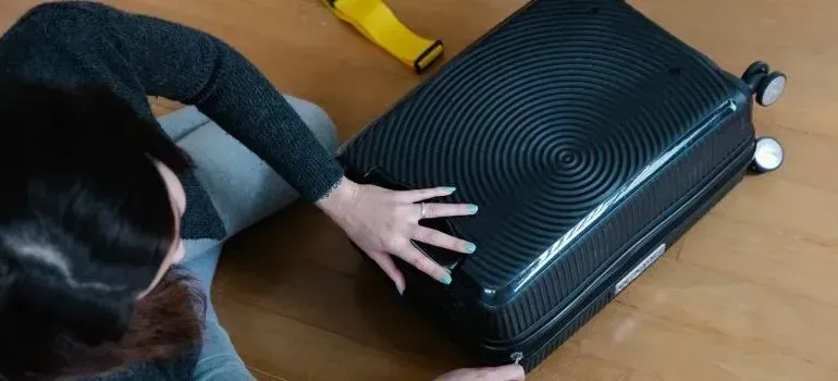 Woman pressing closed black suitcase on wooden floor