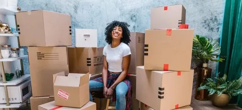 Smiling woman sitting among stacked cardboard moving boxes